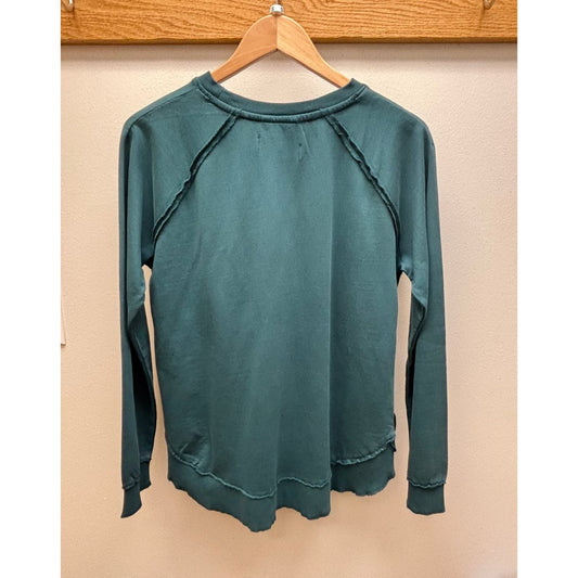 Back view of the Aventura Women's Cotton Drift Crew Neck in Reflecting Pond hanging on a wooden hanger against a beige wall.