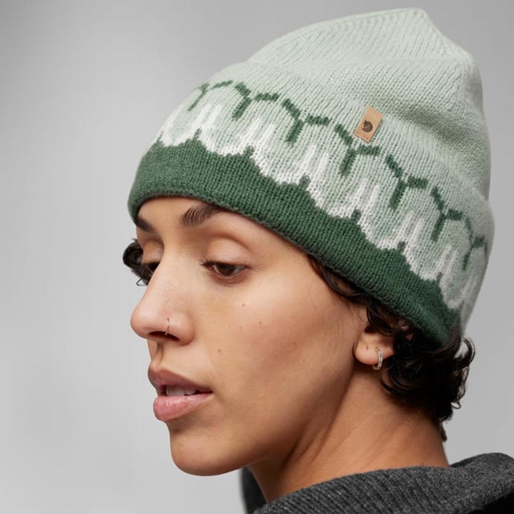 Side view of the Fjallraven Övik Path Knit Beanie in Chalk White Grey with a small leather tag, worn by a model against a plain background.