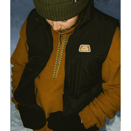 Man wearing the Jetty Port Hi Pile Fleece in Brown with a black vest and beanie, standing on snow.