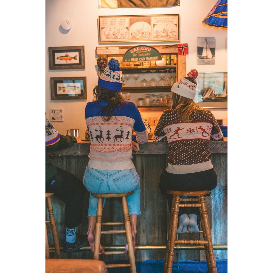 Two women wear Kavu Hillrose in Forage Patch at a wooden bar with framed art on the wall.
