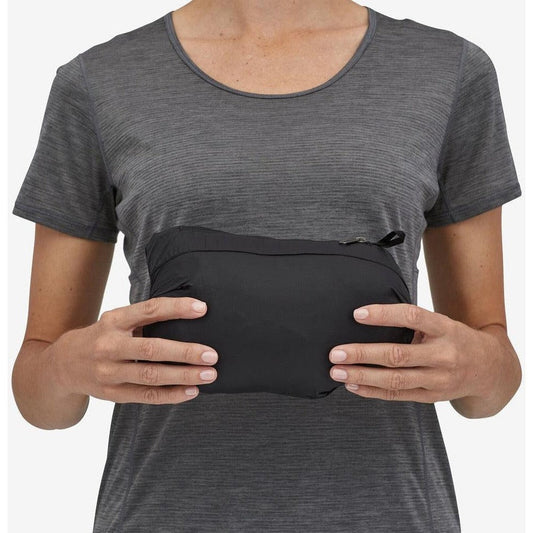 A woman wearing a charcoal Patagonia Women's Down Sweater holds a black pouch in front of her.