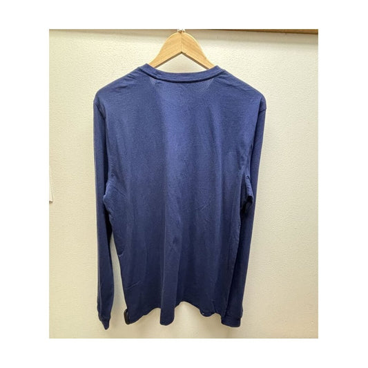 Back view of the Prana Mens Everyday LS Tee-SAMPLE in Capulet Blue hanging on a wooden hanger against a beige wall.
