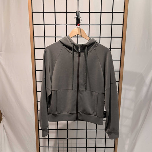 Front view of the Prana Womens Shae Full Zip-SAMPLE in Thyme hanging on a grid wall with a wooden hanger.