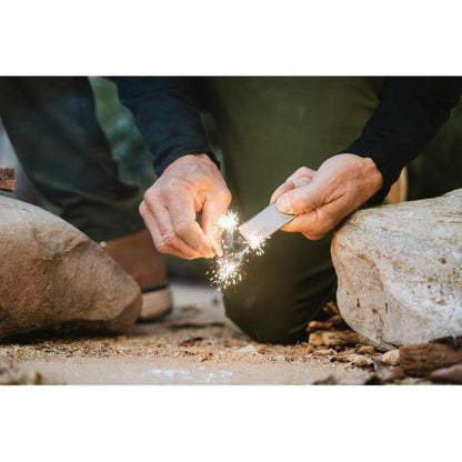A person outdoors uses the Adventure Medical Kits Mag Block to create sparks between two rocks.