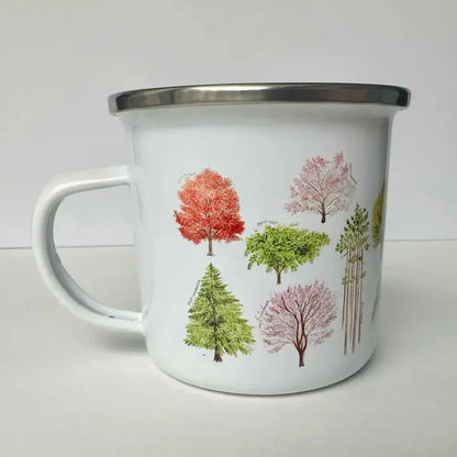 A white Brush & Bark Camping Mug with a silver rim and colorful tree designs sits on a white surface against a plain background.