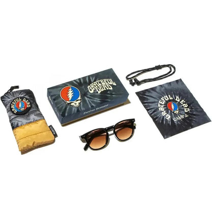 A top-down view of the Camp Eyewear Topo: Grateful Dead Stealie Edition sunglasses and accessories, including a black and gray case, a tie-dye cloth, and a cord, against a white background.