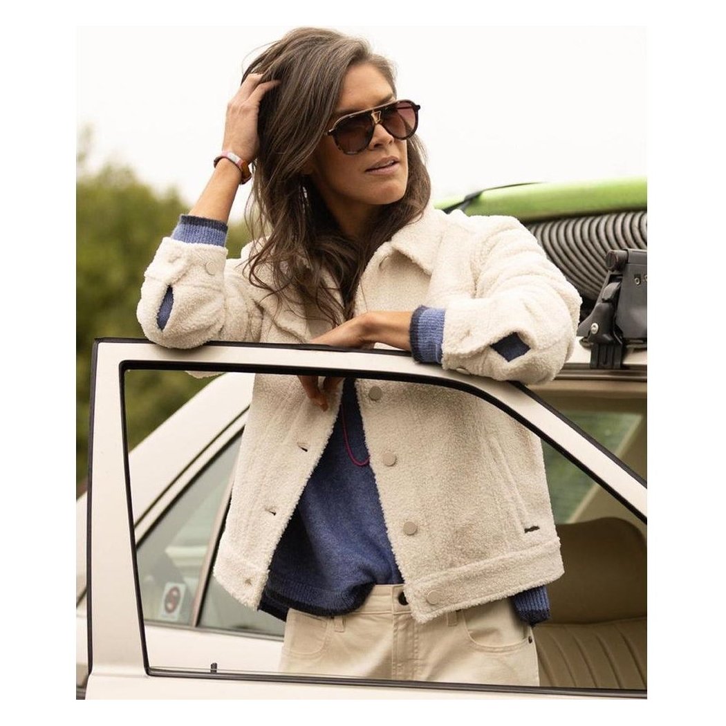 A woman in a Birch Carve Designs Women's Rhea Boucle Trucker jacket leans on a white car door with a green roof rack.
