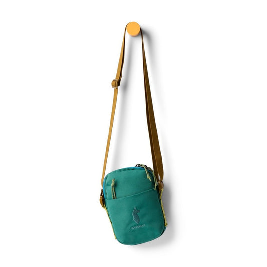 Front view of the Cotopaxi Todo 1L Shoulder Bag in Juniper hanging on a yellow hook against a white background.