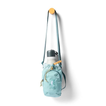 A light blue Cotopaxi Todo Water Bottle Sling hangs from a hook, holding a white water bottle with a charcoal lid, against a plain white background.