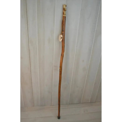 A full-length view of the Creation Carvings Walking Stick with Bear Carving against a light wood-paneled background.