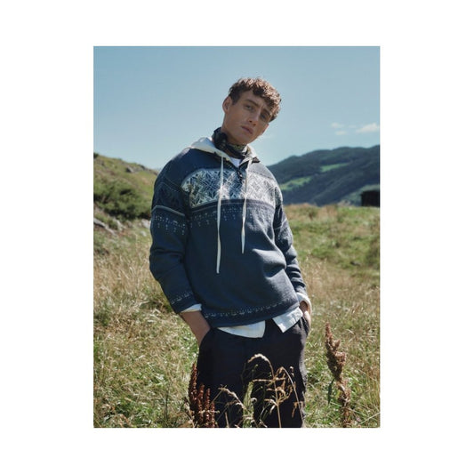 A model wearing the Dale Of Norway Men's Blyfjell Sweater-SAMPLE stands in a grassy field with mountains in the background.
