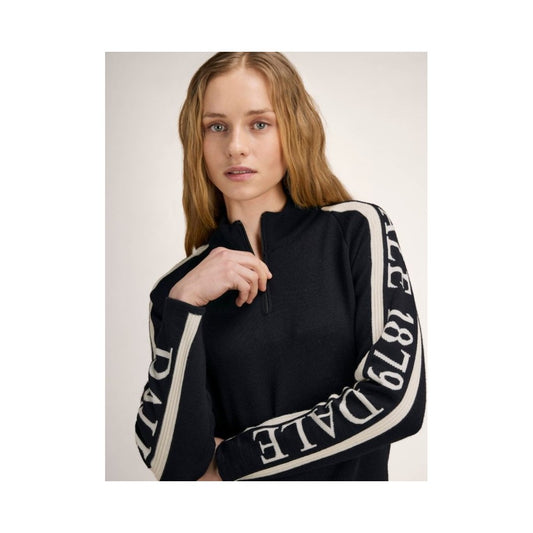 A model wears the Dale Of Norway Skarstind 1879 Feminine Sweater-SAMPLE in BlackOffWhite with white lettering on the sleeves against a light background.