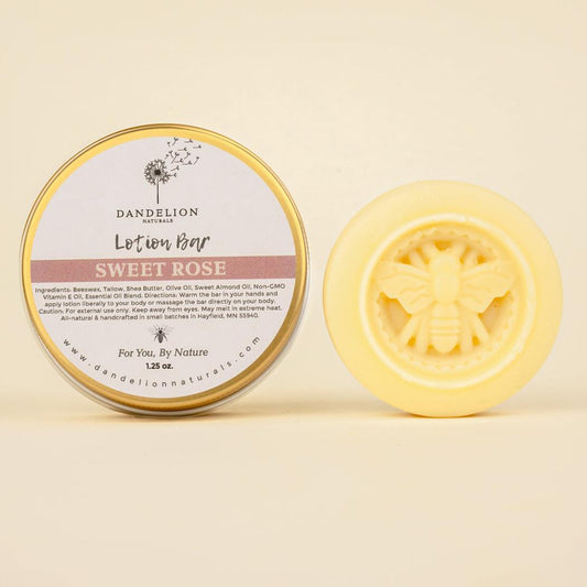 A round tin of Dandelion Naturals Rose Lavender Vanilla Tallow Lotion Bar sits next to a yellow bar with a bee design, both against a light background.