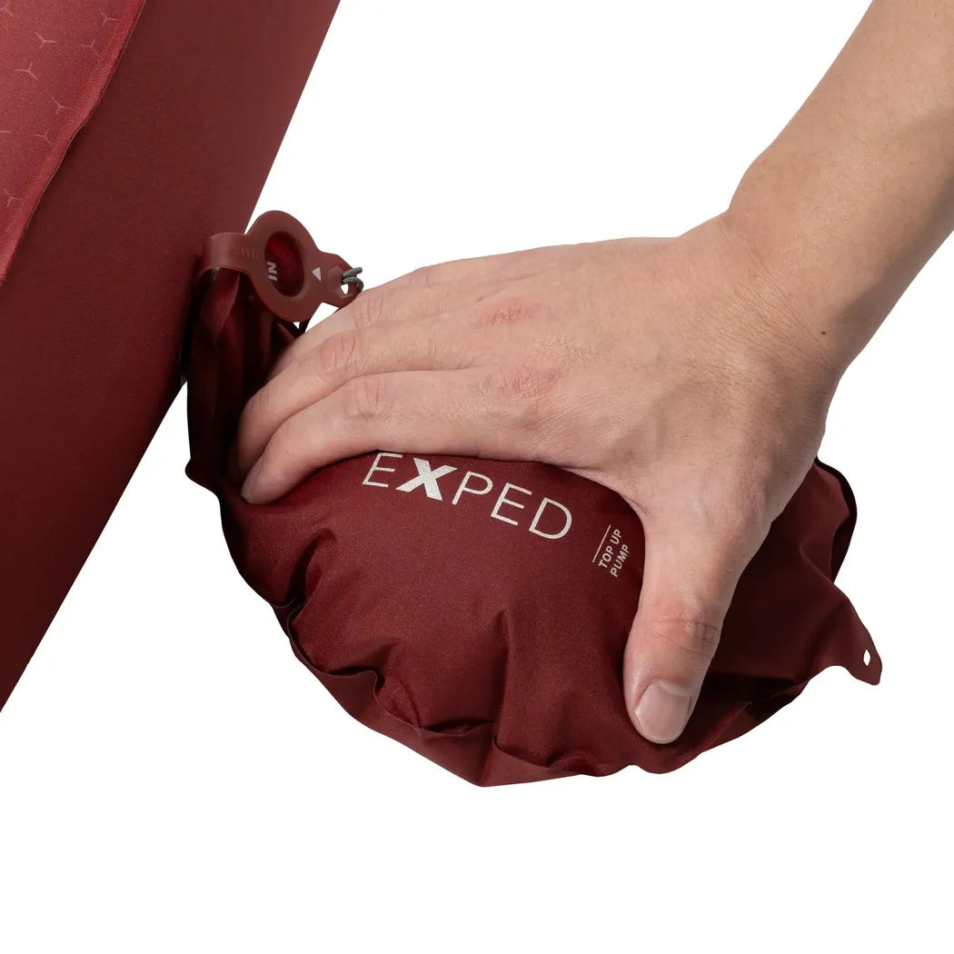 A hand presses down on a burgundy Exped MegaMat Max Duo LW+ sleeping pad attached to a red camping chair.