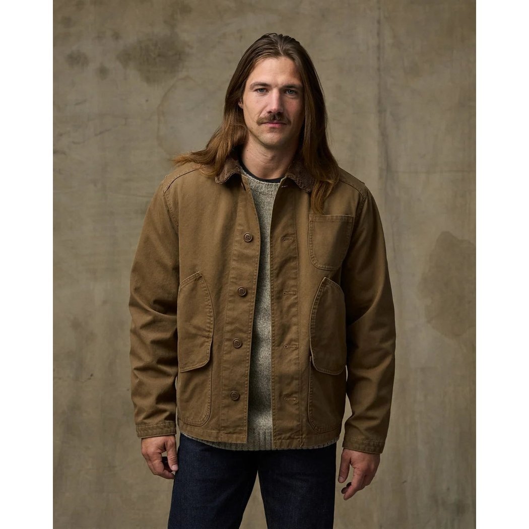 Front view of the Filson Canvas Outfitter Jacket in Kangaroo with a model wearing it against a textured background.