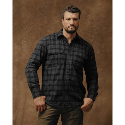 Front view of the Filson Men's Alaskan Guide Shirt in Heath Blk Plaid with a model wearing it against a brown background.