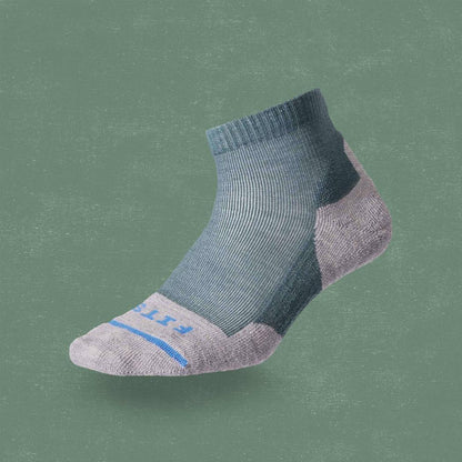 A side view of the FITS Light Hiker Quarter sock in Coal color on a green background.