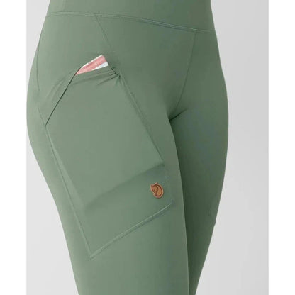 Side view of the Fjallraven Women's Abisko Tights in Patina Green showing the large front pocket with a card inside against a plain background.