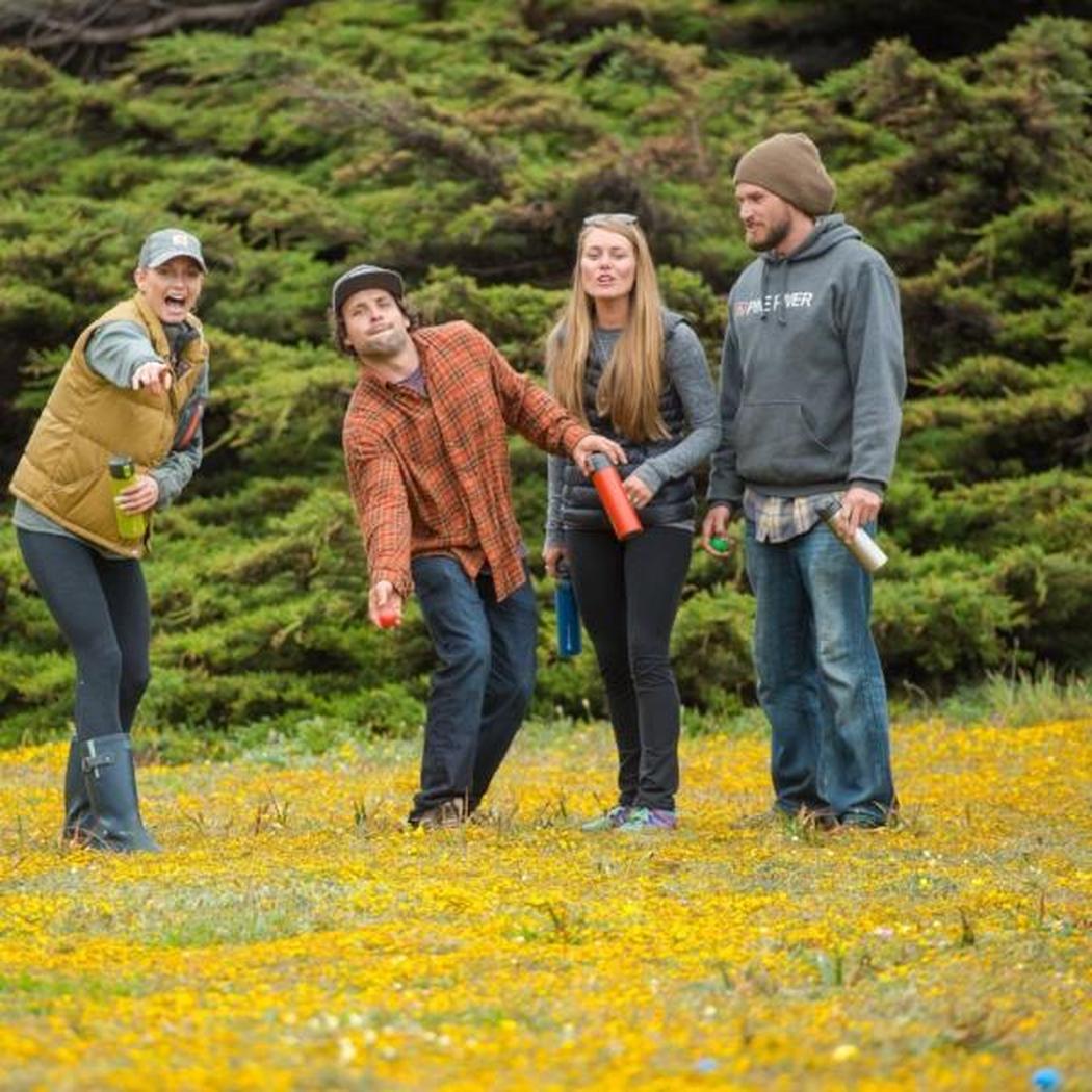 Four people play bocce in a field of yellow flowers wearing GSI Outdoors Backpack Bocce in Assorted colors.