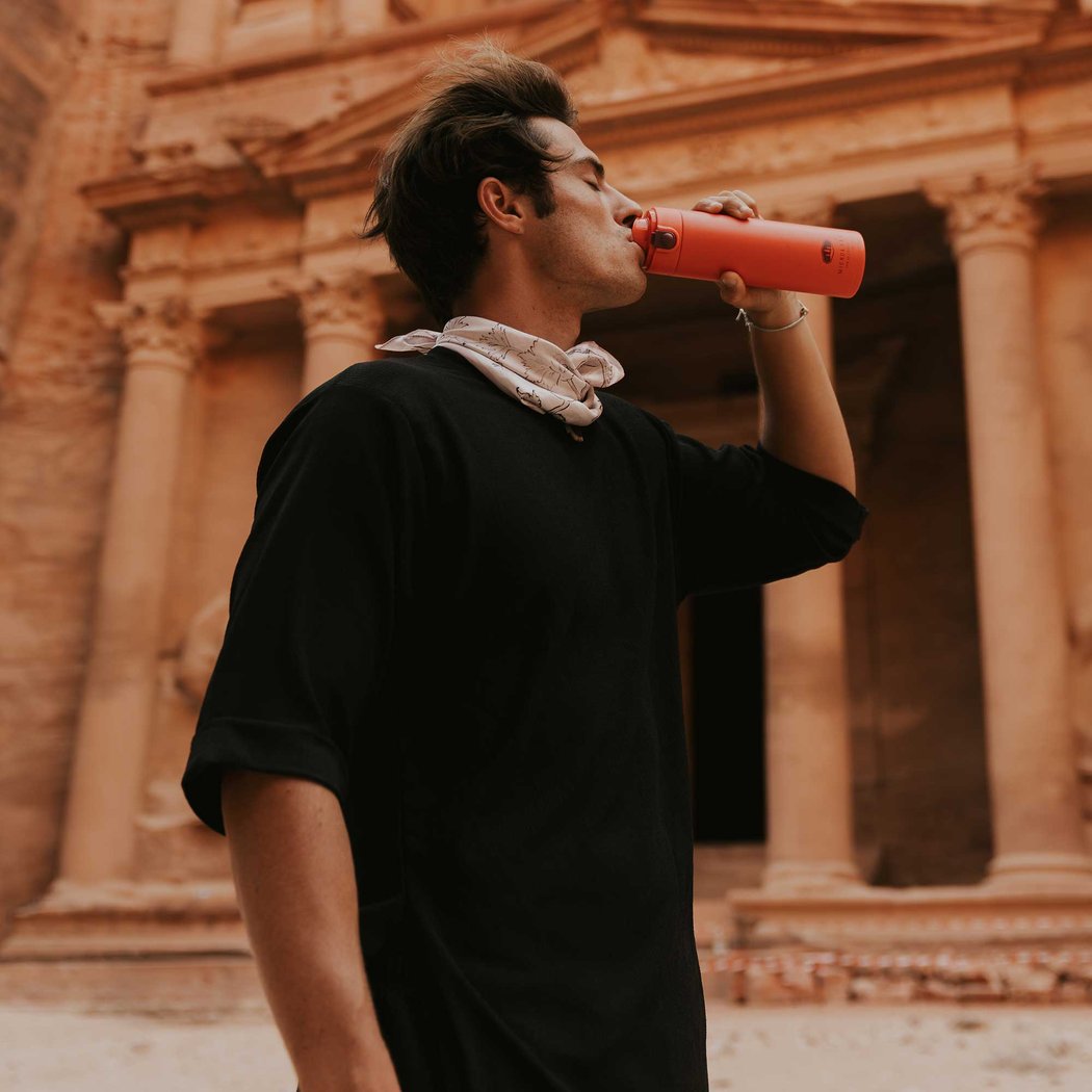 Model in black shirt drinks from an amethyst GSI Outdoors Microlite 500 Flip water bottle in front of a stone building.