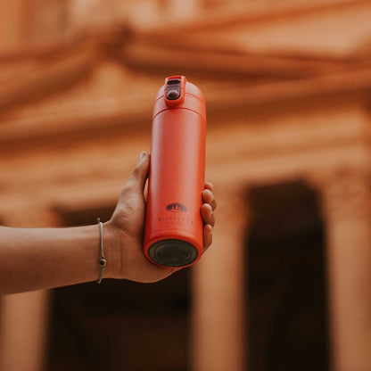 Hand holding the GSI Outdoors Microlite 500 Flip in amethyst against a blurred architectural background.