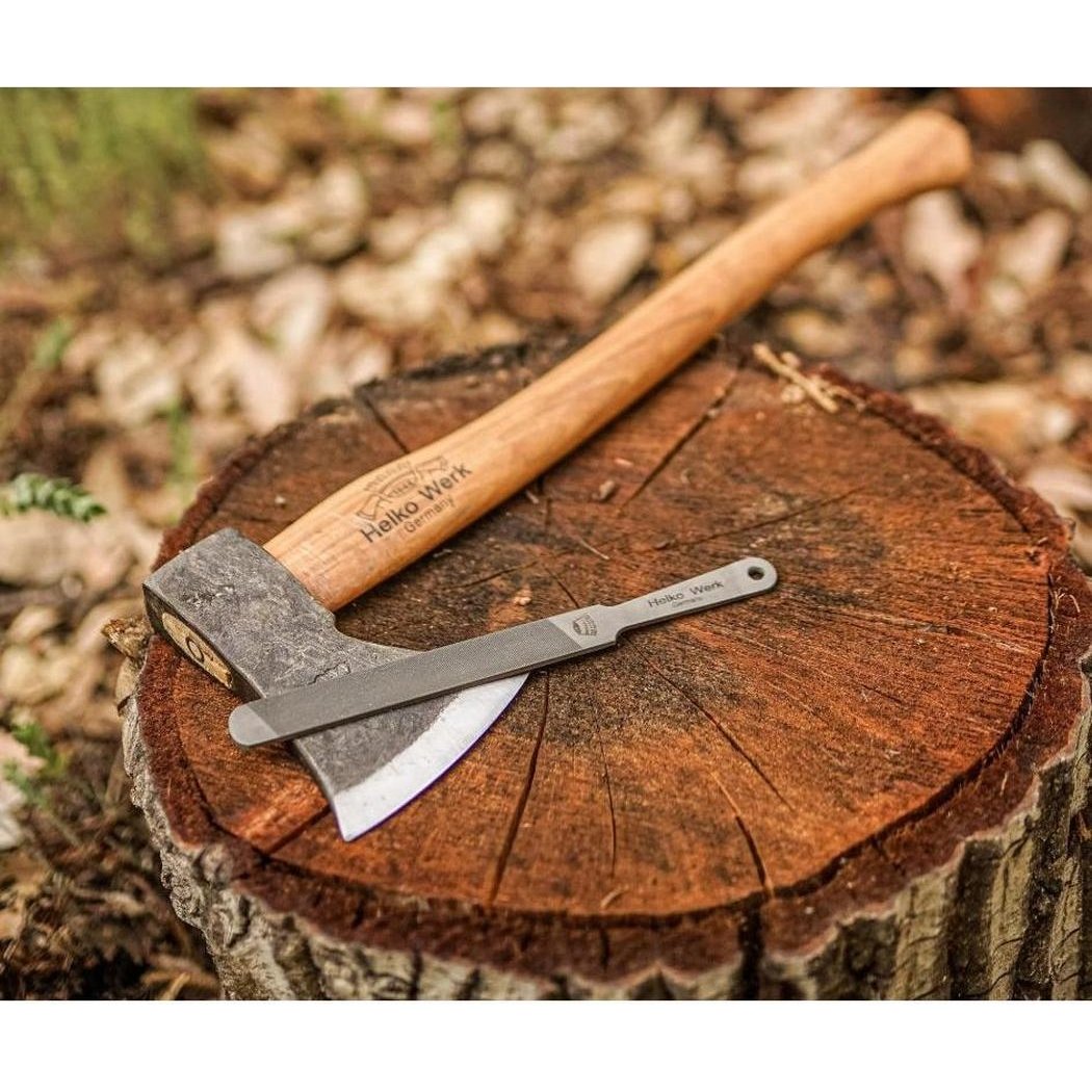 A Helko Werk Compact Sharpening File rests on a wooden axe atop a tree stump in a forest setting.