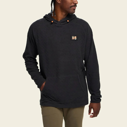 A man wearing the Howler Brothers Men's Palo Duro Fleece Hoodie in Antique Black stands against a plain background.