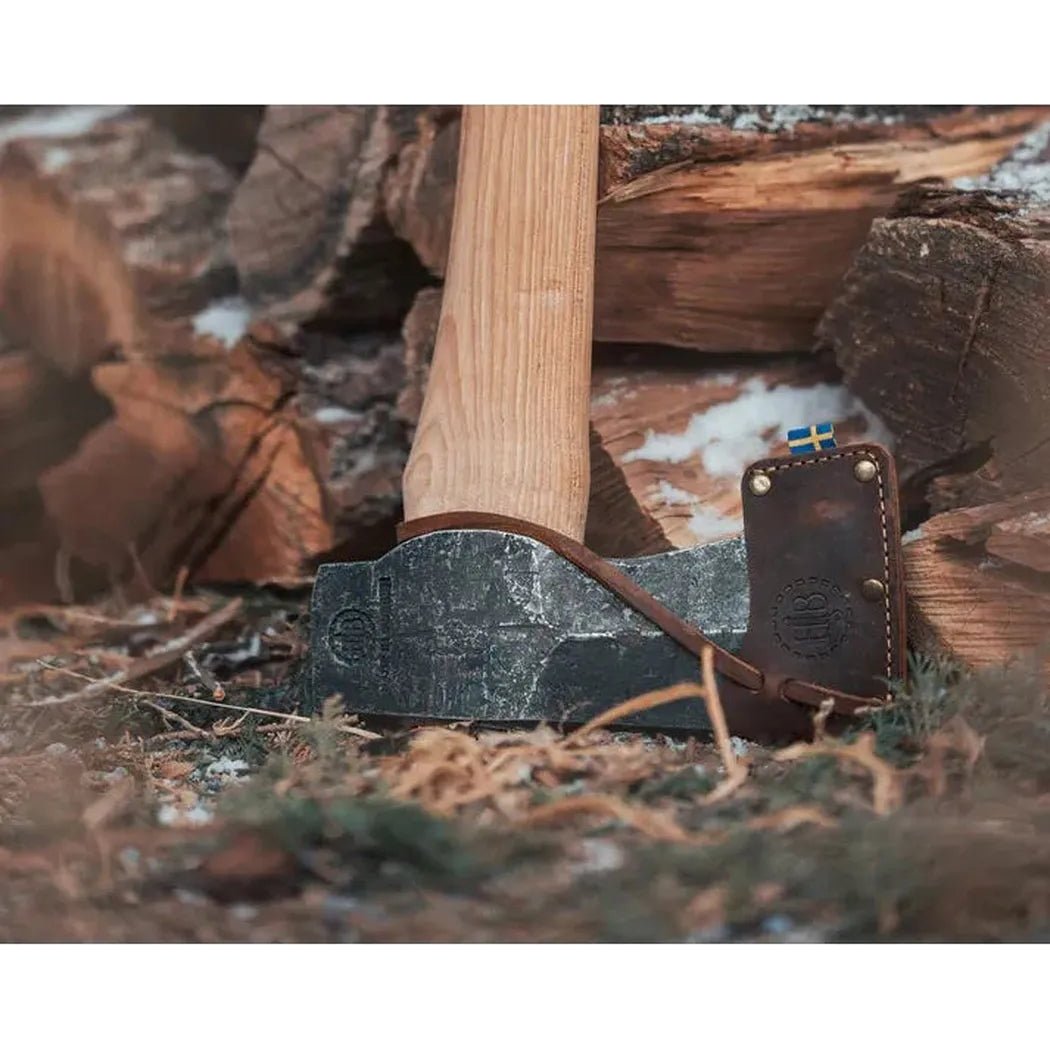 A close-up of the Hults Bruk Kvillinge Splitting Axe with its wooden handle and charcoal-colored blade resting on a pile of firewood.