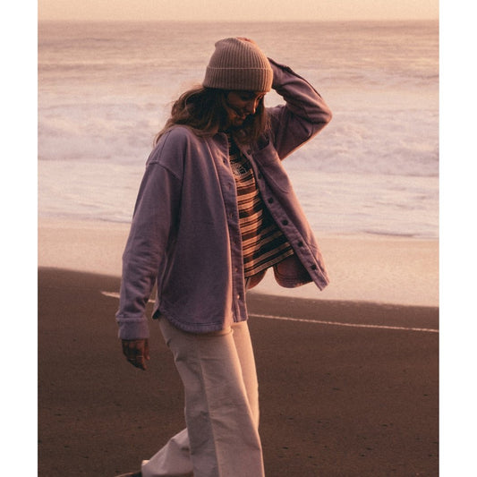 Model wearing the Jetty Eden Knit Shirt in Seafog on a beach at sunset with waves in the background.