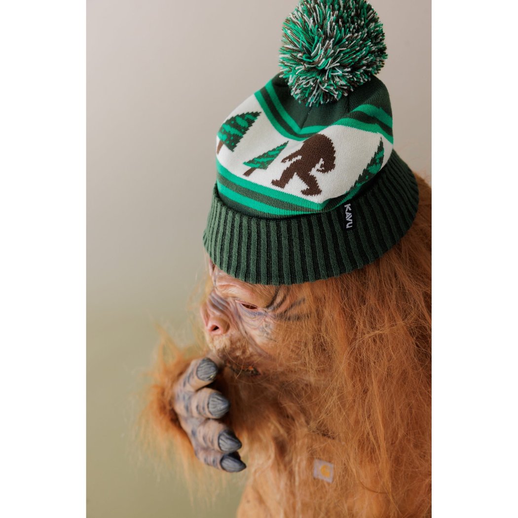 Side view of the Kavu Herschel in Squirrely with a model wearing it and a green pom-pom.
