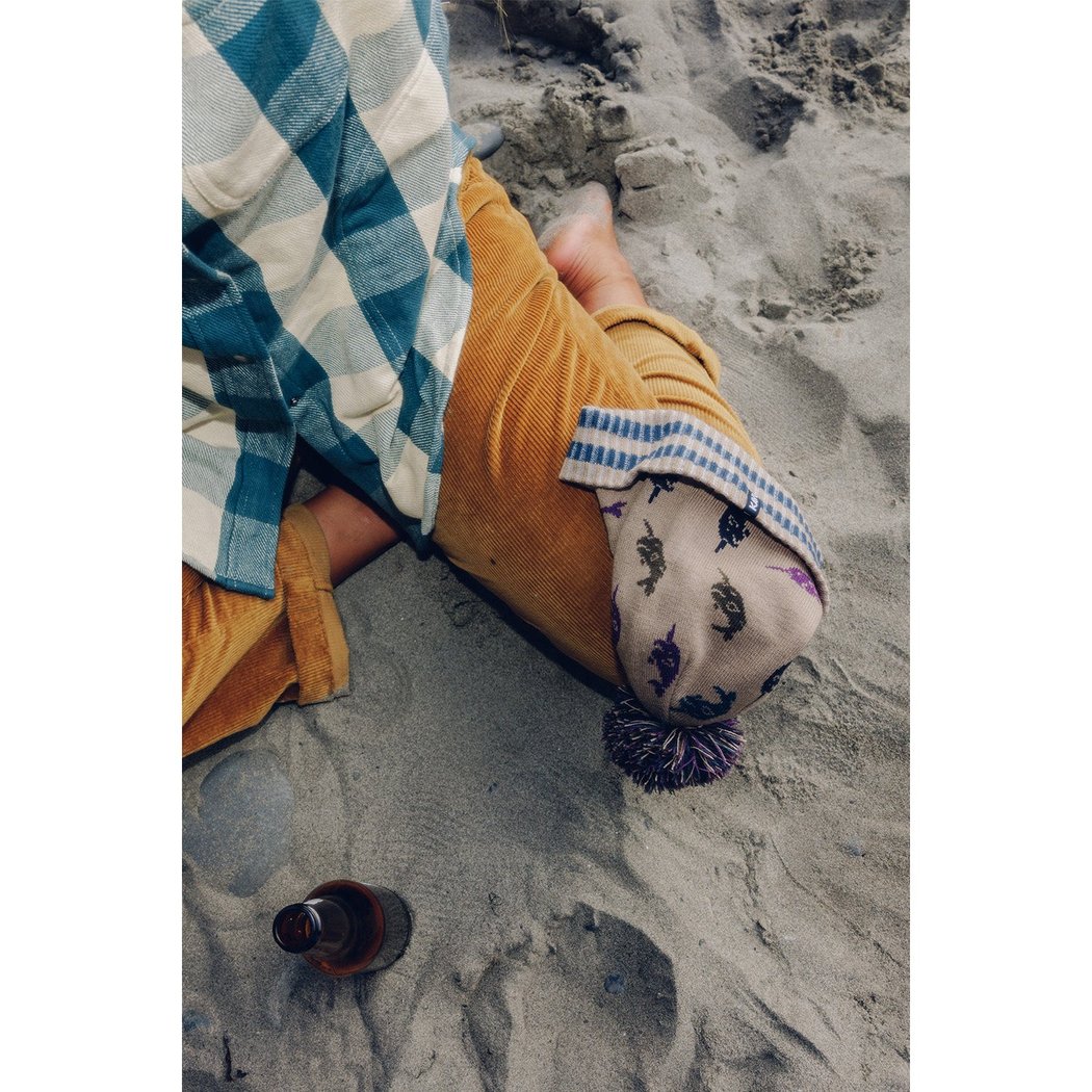 Top-down view of the Kavu Herschel in Squirrely on a sandy beach with a bottle nearby.