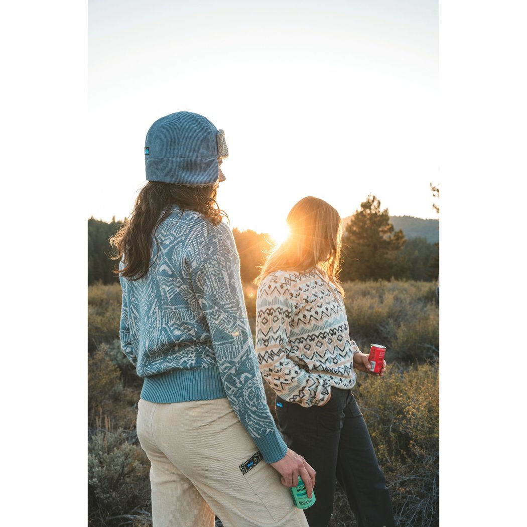Two women wear the Kavu Wood Valley in Big Bear while walking in a sunlit field with trees and hills in the background.