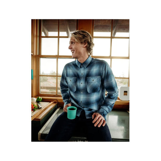 Man in Faded Demin Kuhl Men's Dillingr Flannel Long Sleeve sitting by a window with a teal mug.