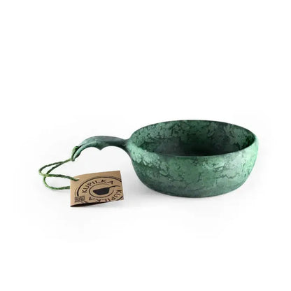 A black Kupilka 55 Soup Bowl with a handle sits on a white background next to a tag.