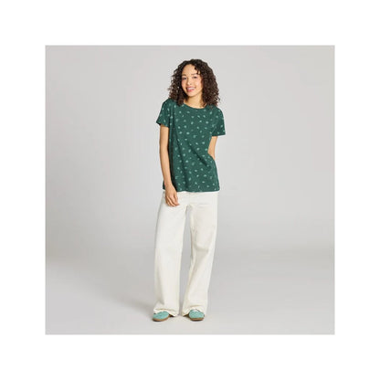 A model wears the Life is Good Women's Falling Leaves Pattern Crusher in Treeline Green with white pants against a gray background.