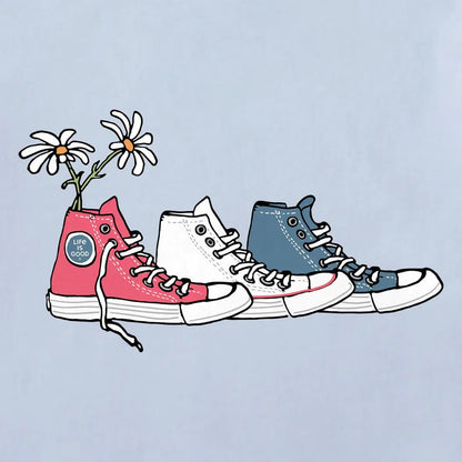 A front view of the Life is Good Women's Patriotic Daisy Sneakers Short Sleeve Tee in Glacier Blue with a light blue background.