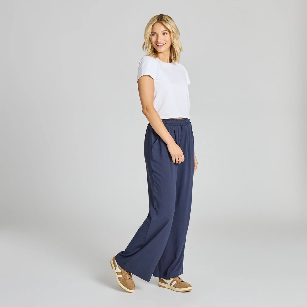 Side view of the Life is Good Women's Solid Breezy Wide Leg Pant in Inkwell Blue on a model against a light gray background.