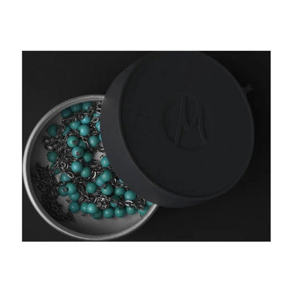 A top-down view of the Matador Waterproof Travel Canister - 100ml with its lid open, revealing turquoise beads inside against a dark background.