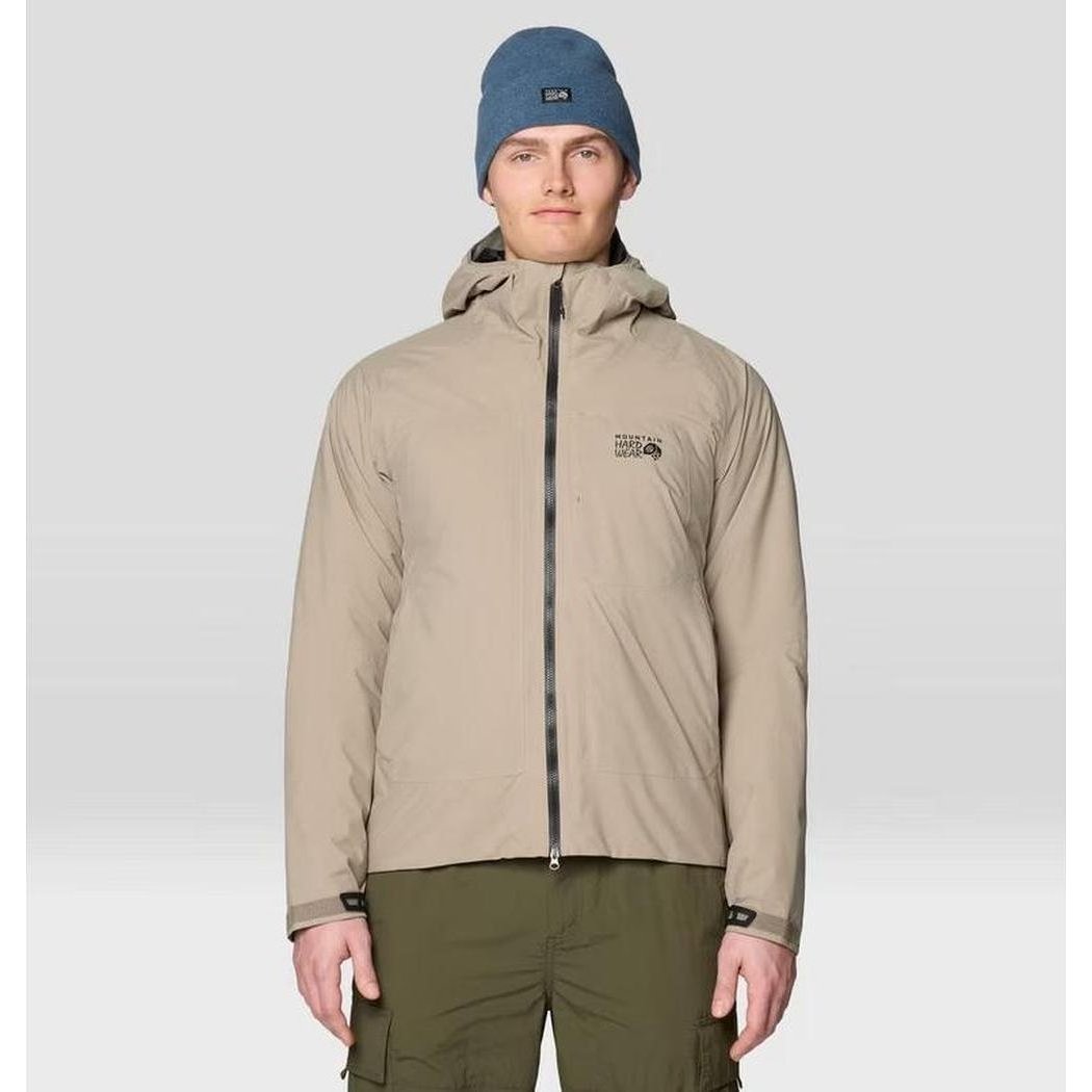A front view of the Mountain Hardwear Men's Stretch Ozonic Insulated Jacket in Dunes on a model wearing olive cargo pants and a blue beanie against a light gray background.