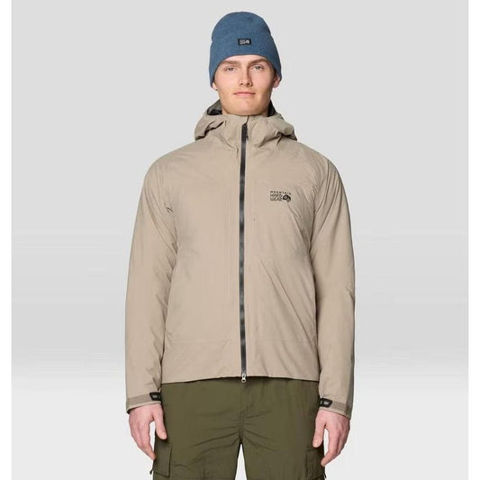 A front view of the Mountain Hardwear Men's Stretch Ozonic Insulated Jacket in Dunes on a model wearing olive cargo pants and a blue beanie against a light gray background.