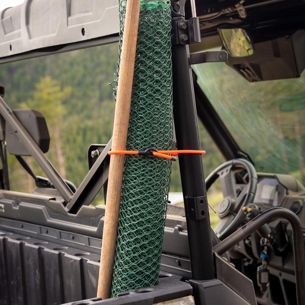 A roll of green netting and a wooden stick are secured with a bright orange Nite Ize Gear Tie Loopable Twist Tie 24 inch on a black metal post of an off-road vehicle.