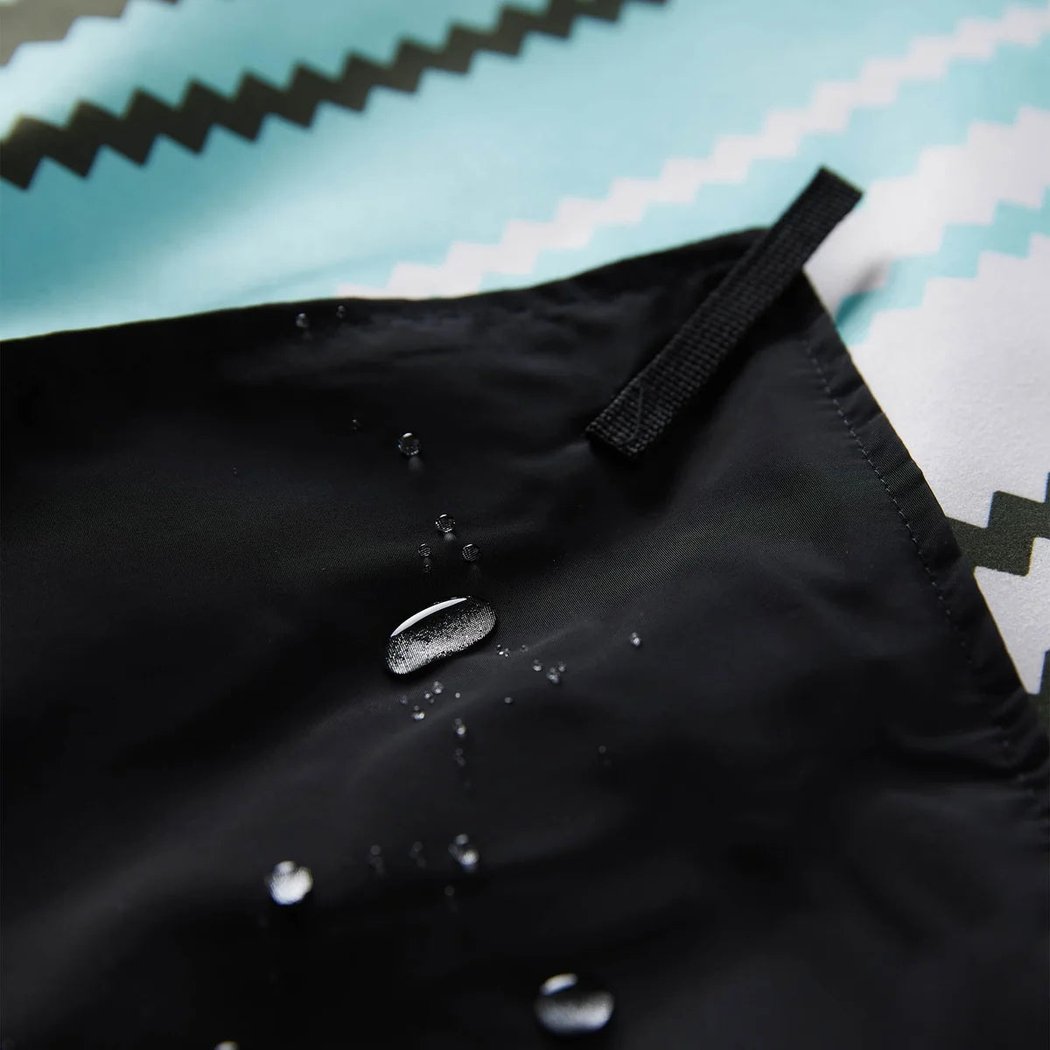 Close-up of the Nomadiz Festival Blanket in Baja Aqua showing water droplets beading on its black edge against a patterned background.