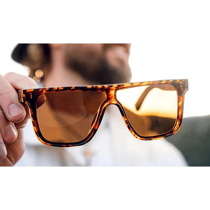 A hand holds the Shiny Black + Wood Optic Nerve Mojo sunglasses with a blurred outdoor background.
