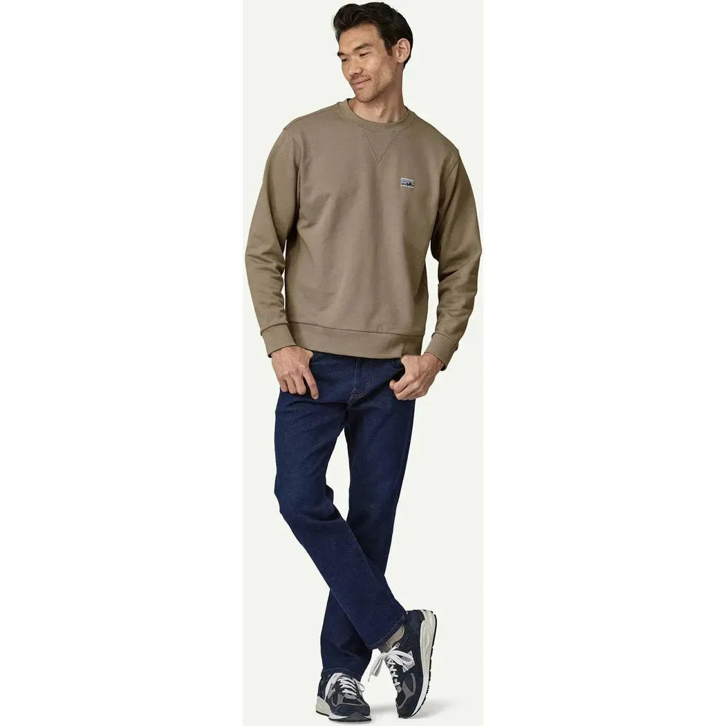 A model wearing the Patagonia Men's Daily Crewneck Sweatshirt in Seabird Grey stands with one leg crossed against a plain white background.