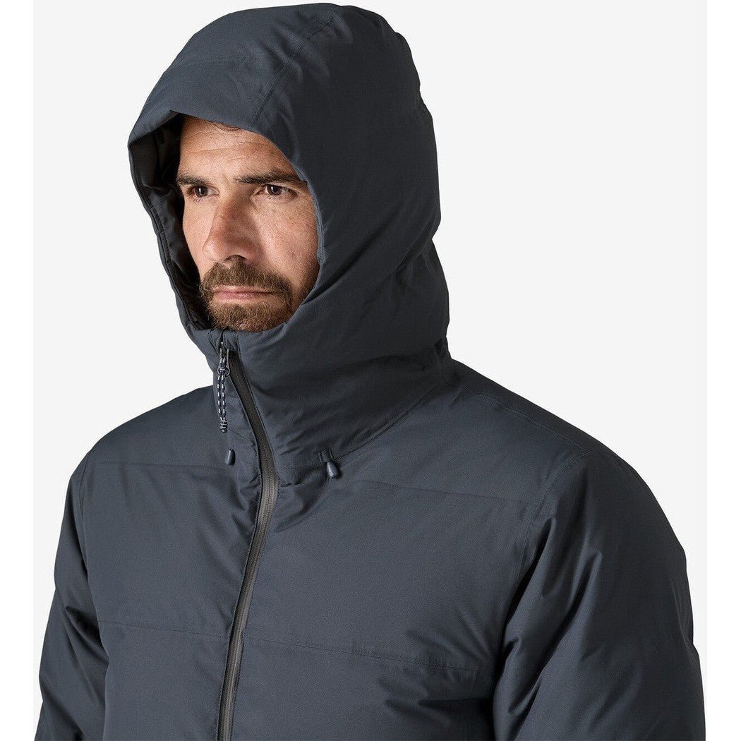 A man wearing the Patagonia Men's Jackson Glacier Parka in Black with a hood up against a white background.