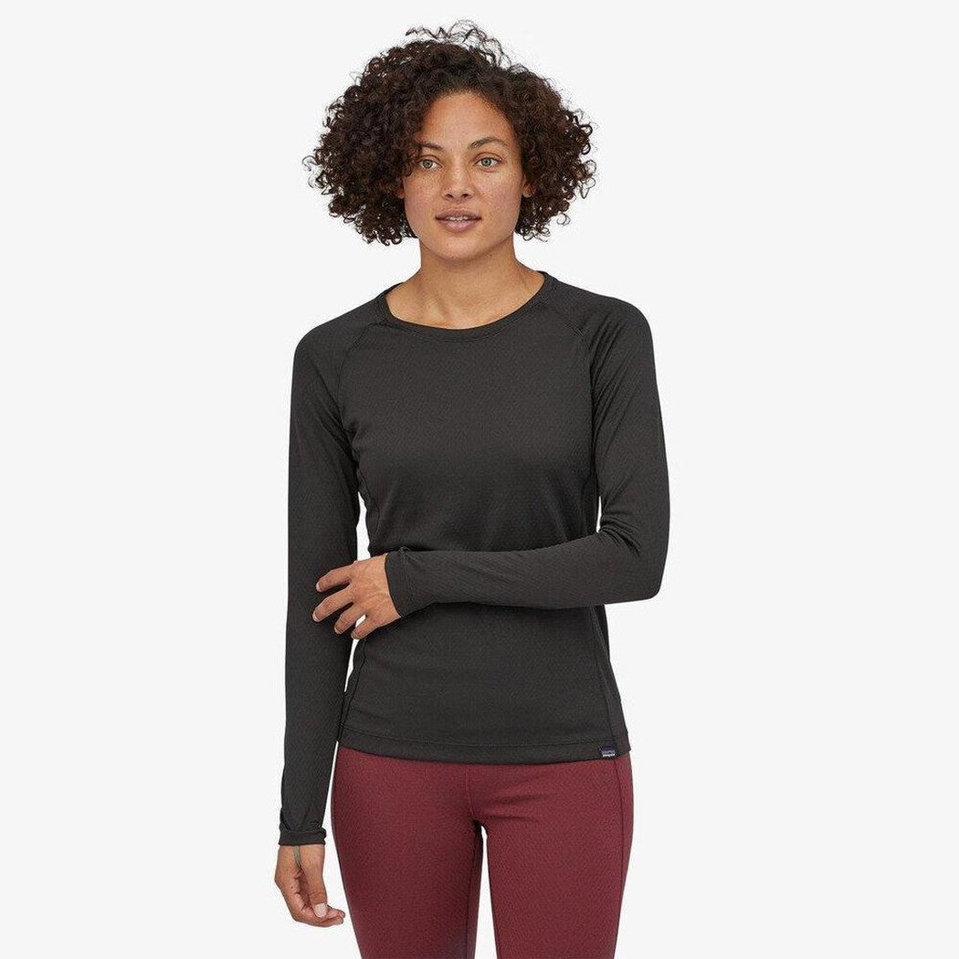 A woman wearing the Patagonia Women's Capilene Midweight Crew in Black stands against a plain white background.