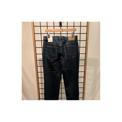 Back view of the Prana Mens Carlsbad 760 Standard Jean-SAMPLE in Lagoon/32 hanging on a wooden hanger against a grid background.