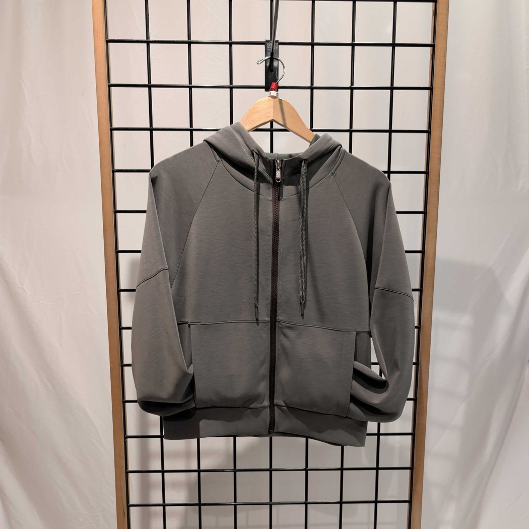 Front view of the Prana Womens Shae Full Zip-SAMPLE in Thyme hanging on a wooden hanger against a grid background.