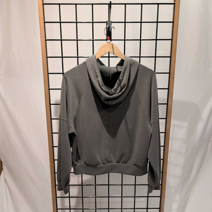 Back view of the Prana Womens Shae Full Zip-SAMPLE in Thyme hanging on a wooden hanger against a grid background.