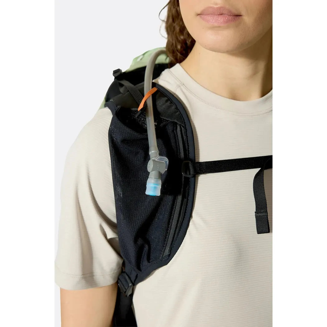 A woman wears the Rab Airox 22ND backpack with a visible hydration tube and black straps against a plain white background.